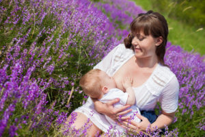 Mother breastfeeding her baby in a field of purple flowers